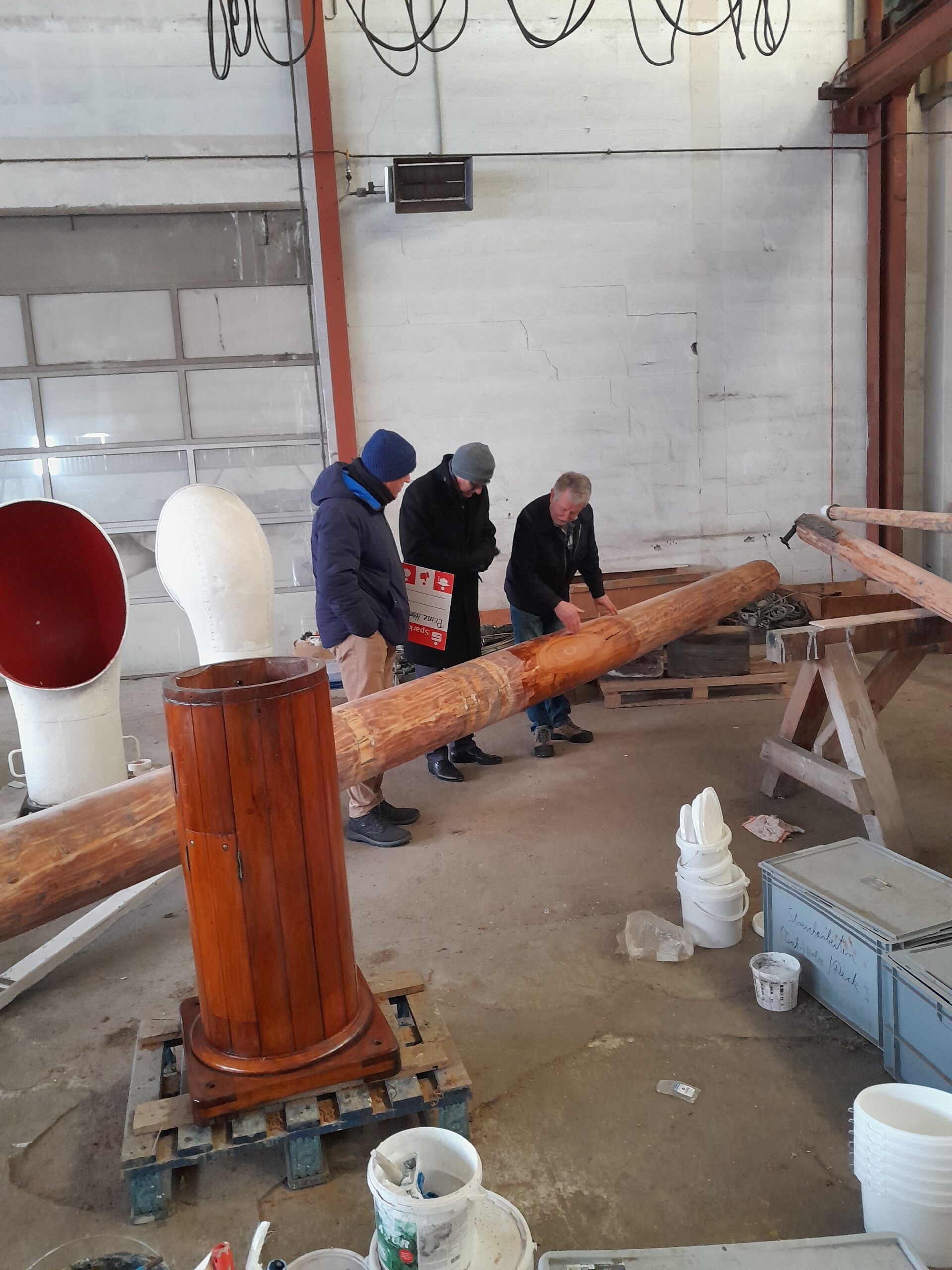 Drei Männer stehen um eine flach liegenden Masten.