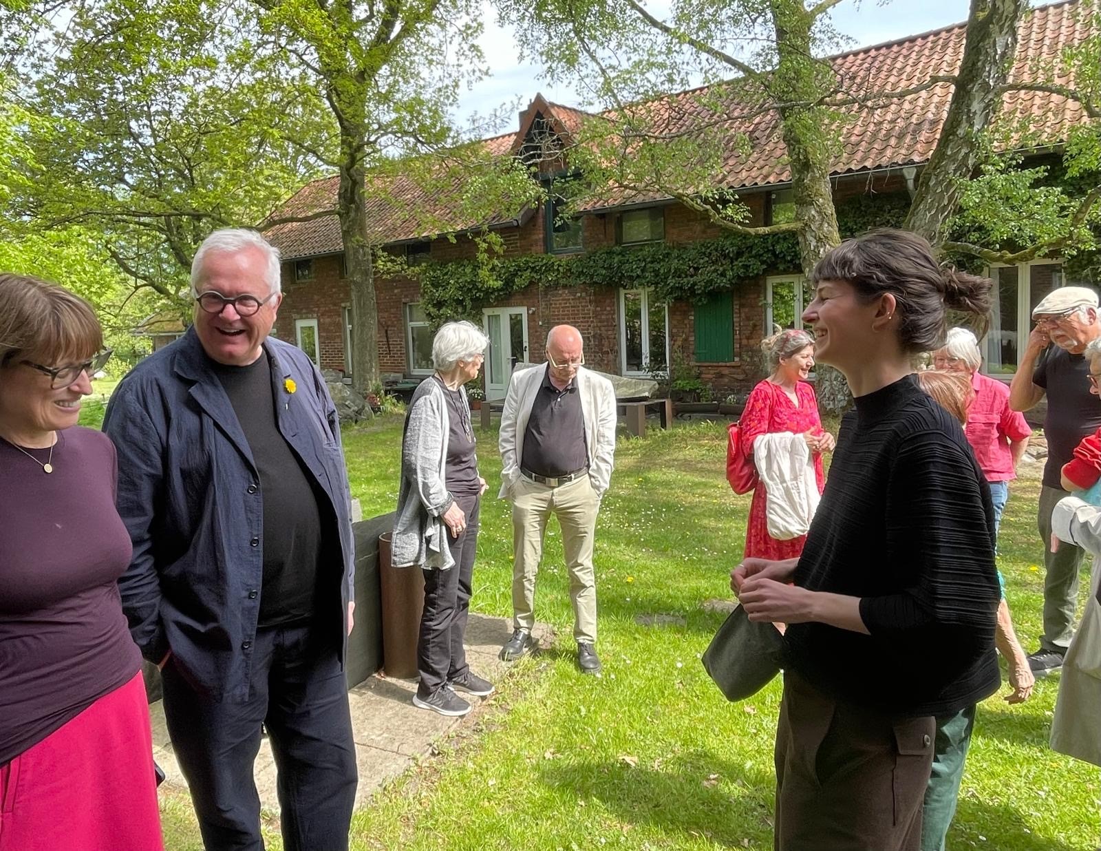 Die Künstlerin Ana Maria Szöllösi steht im Garten des Springhornhofs und befindet sich im gespräch mit mit Bettina v. Dziembowski und dem Vorstand des Springhornhofs, Prof. Dr. Martin Warnke